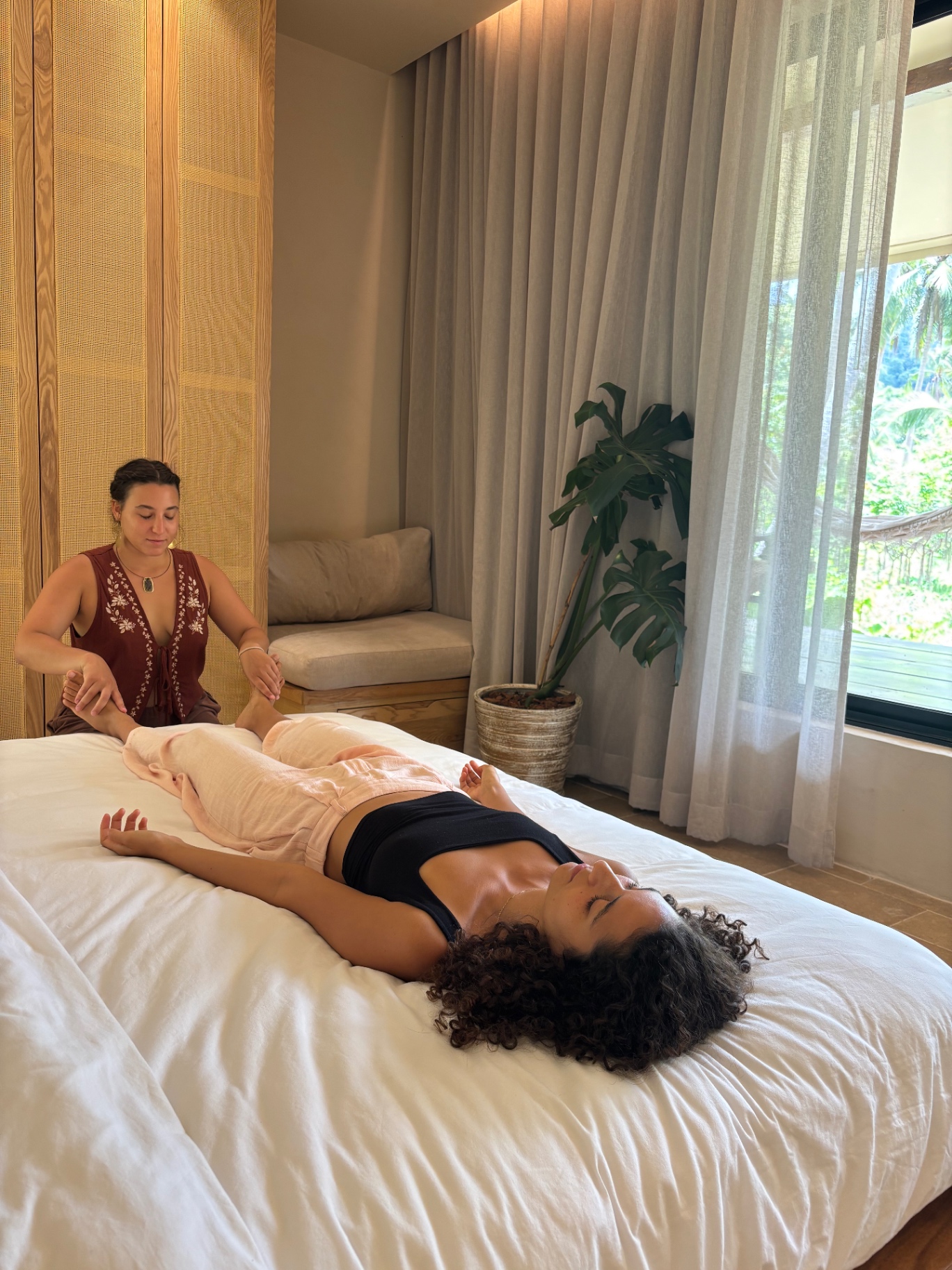 A quiet treatment room — the client resting fully as the practitioner works at the feet